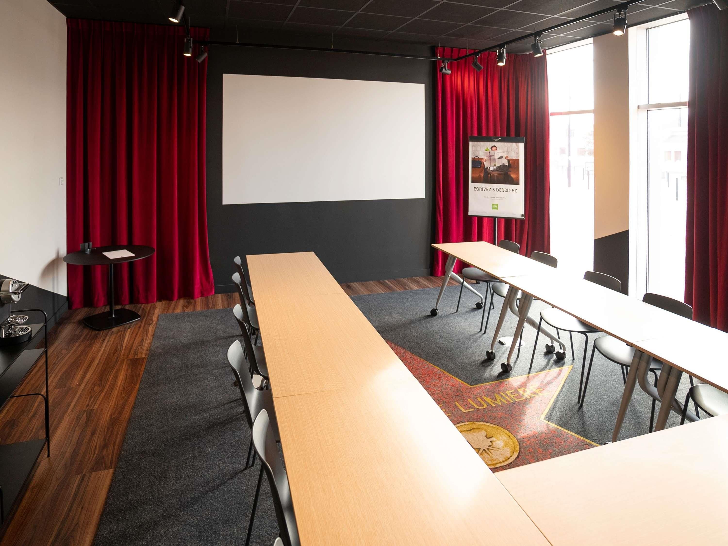 Une salle de conférence avec une longue table, des chaises, un écran de projection et des rideaux rouges.