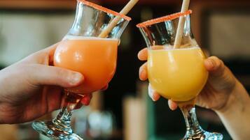 Two people holding glasses with straws, one with an orange drink and one with a yellow drink.