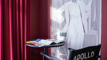 A room with red curtains, a table with papers, and a poster of a man in a suit.