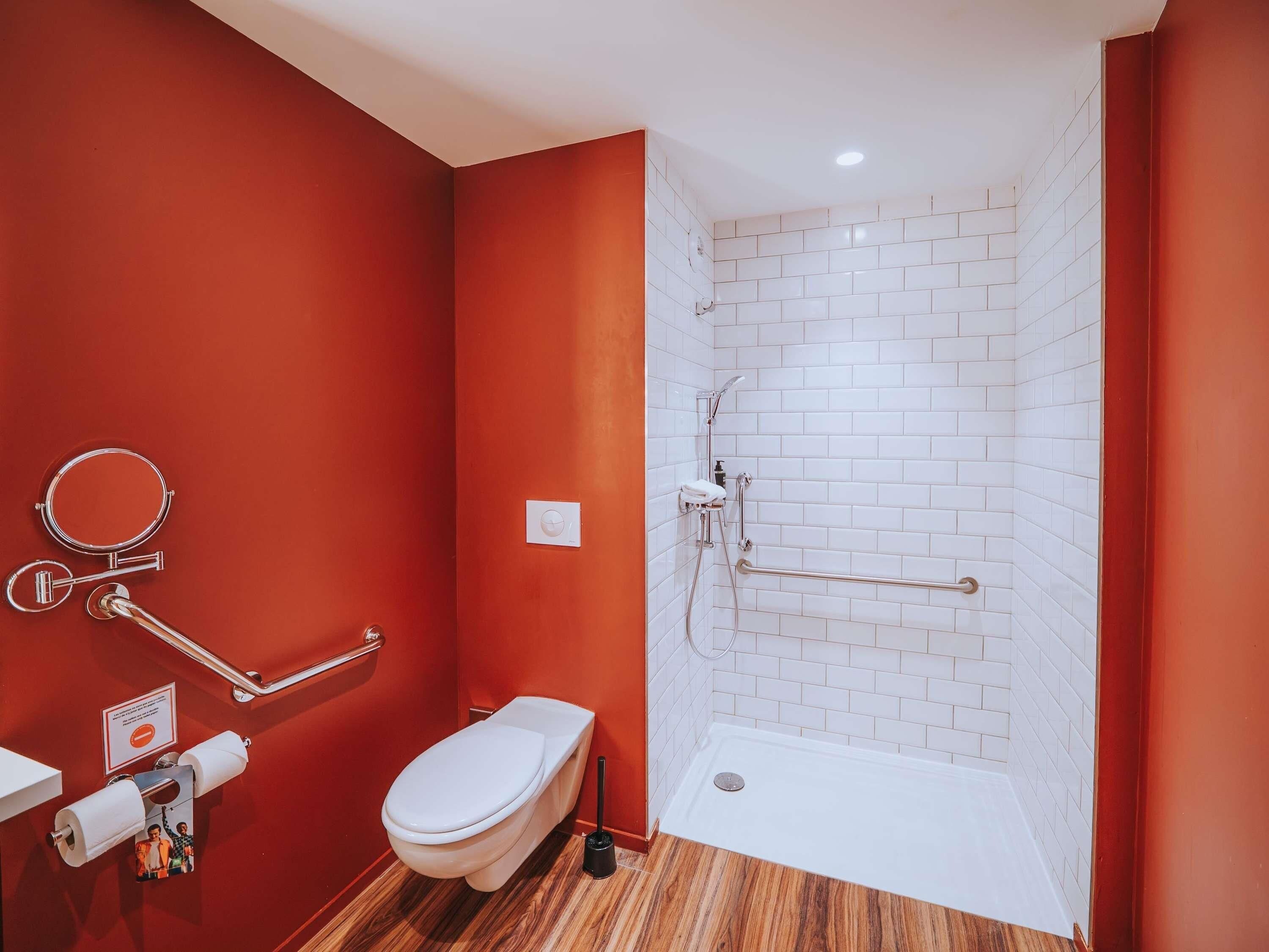 Une salle de bain avec des toilettes blanches, une douche avec un mur recouvert de carreaux blancs et un plancher en bois.