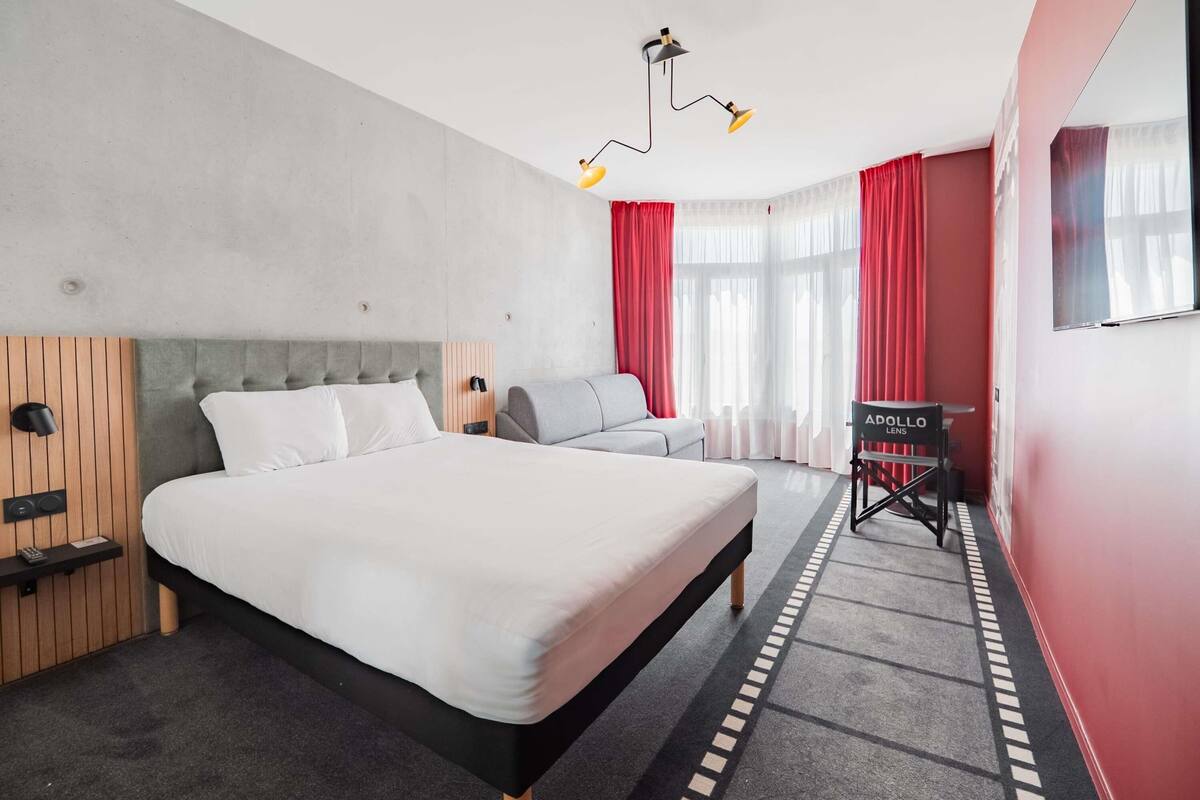 A modern hotel room with a large bed, a seating area, a desk, and a TV.
