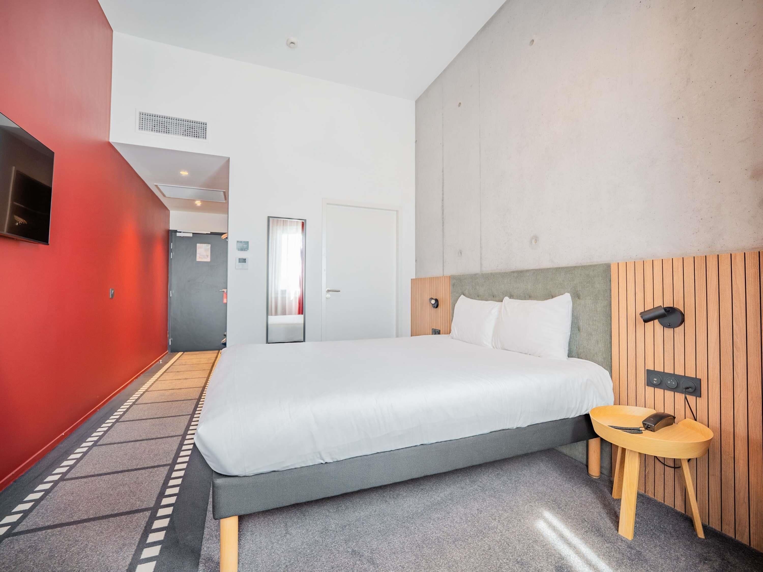 Una habitación de hotel con una cama, una mesita de madera, un espejo y una pared roja.