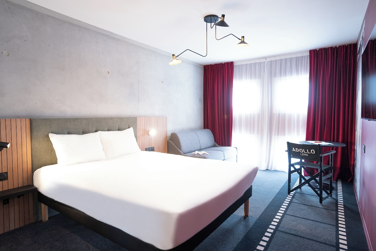 A hotel room with a large bed, a sofa, a desk, and a chair.