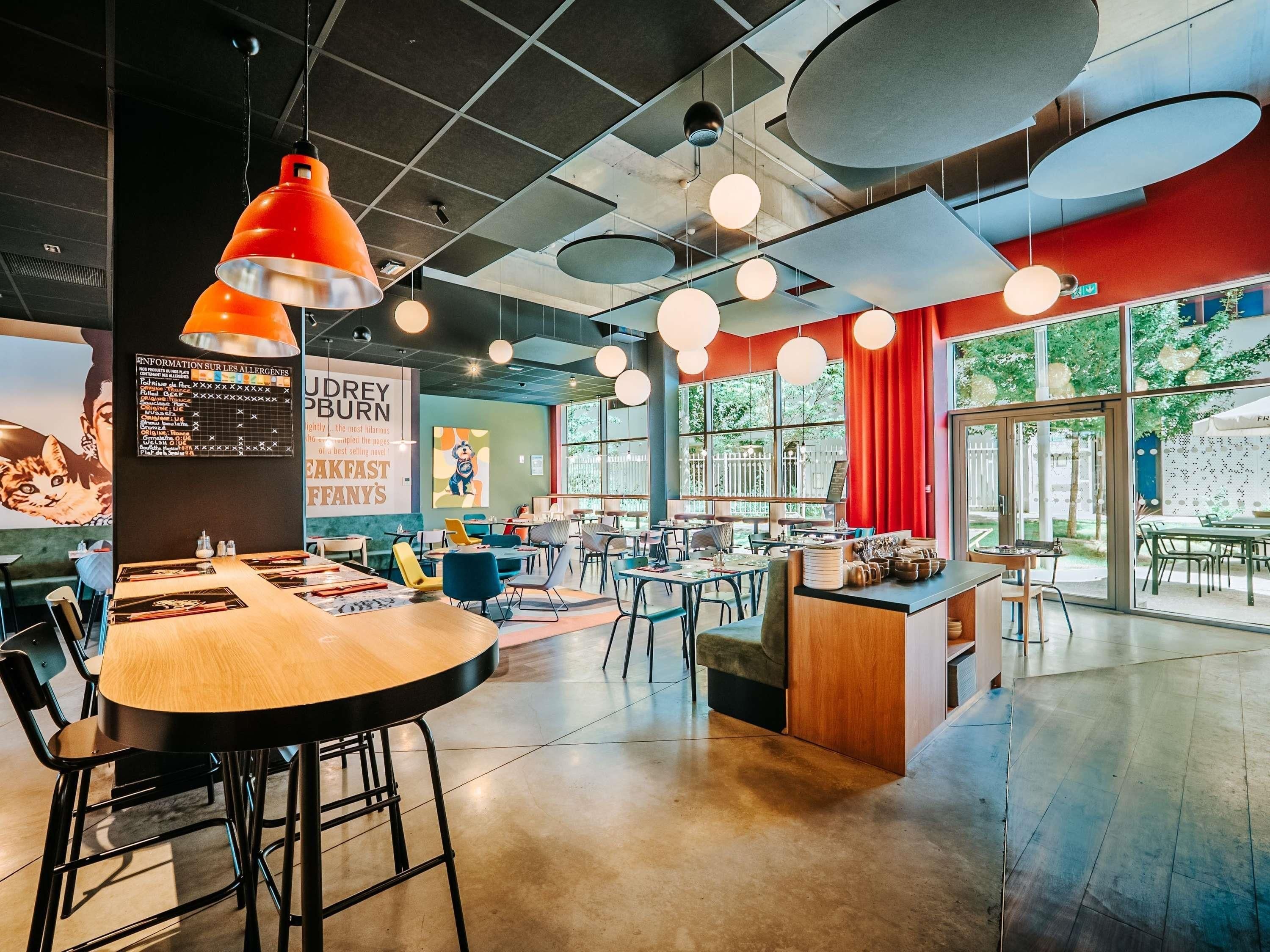 Un restaurante moderno con mesas redondas, lámparas colgantes y amplios ventanales.