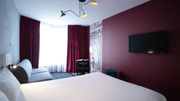 A hotel room with a large bed, a flat-screen TV mounted on the wall, and a desk with a lamp.