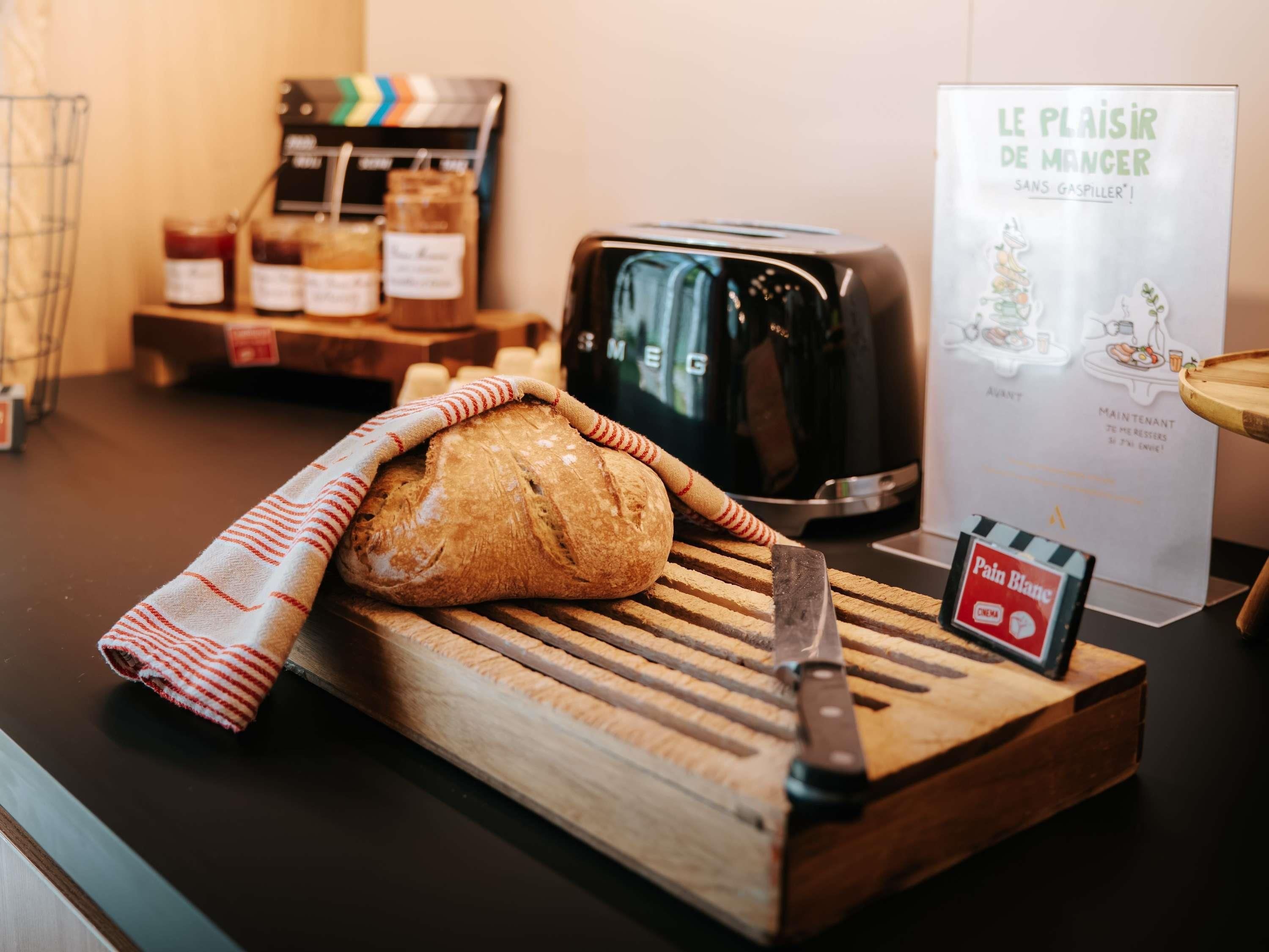 Un piano di lavoro in cucina con una pagnotta di pane su un tagliere di legno, un coltello, un tostapane e un cartello con un personaggio dei cartoni animati.