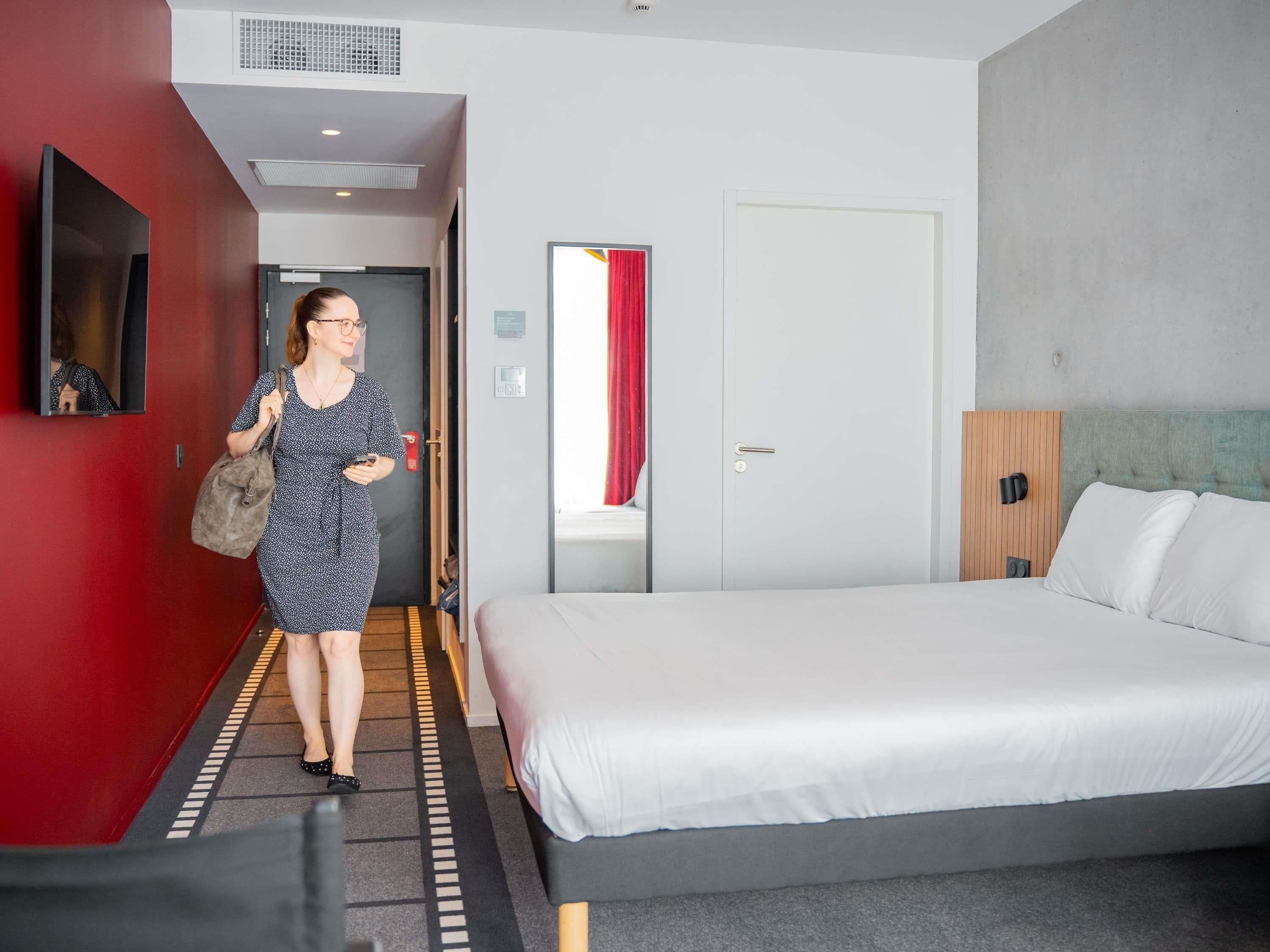Une chambre d’hôtel avec un lit, une armoire, un miroir et un mur rouge.