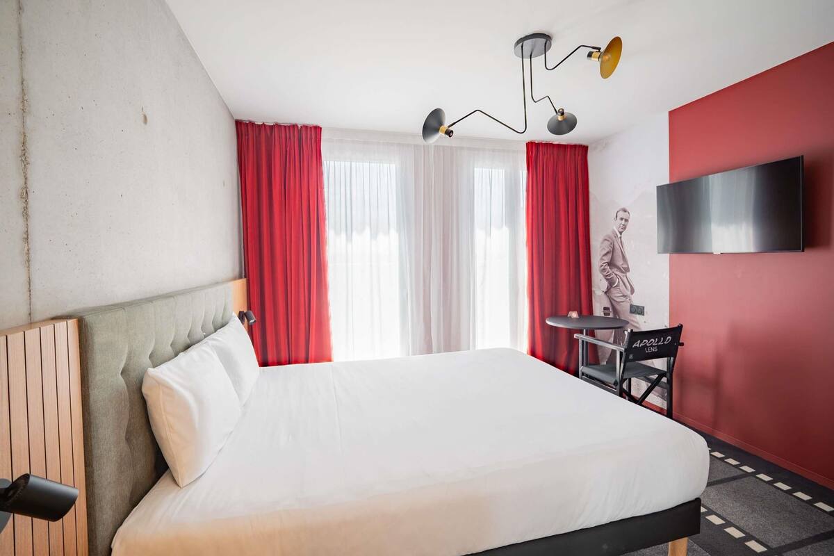 A hotel room with a bed, a desk, a chair, a statue, and a TV on the wall.