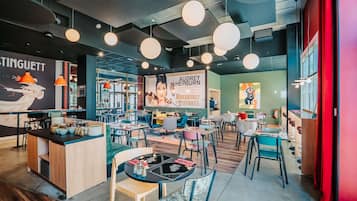 L’intérieur d’un café moderne, avec des luminaires suspendus de forme ronde, un comptoir avec des tabourets et une fresque publicitaire représentant Audrey Hepburn.