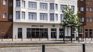 Un edificio moderno con un llamativo letrero 'APOLLO', que cuenta con un bar llamado 'APOLLO BAR' a nivel de calle.