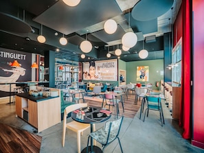 A modern cafe interior with round pendant lights, a counter with stools, and a mural advertising Audrey Hepburn.