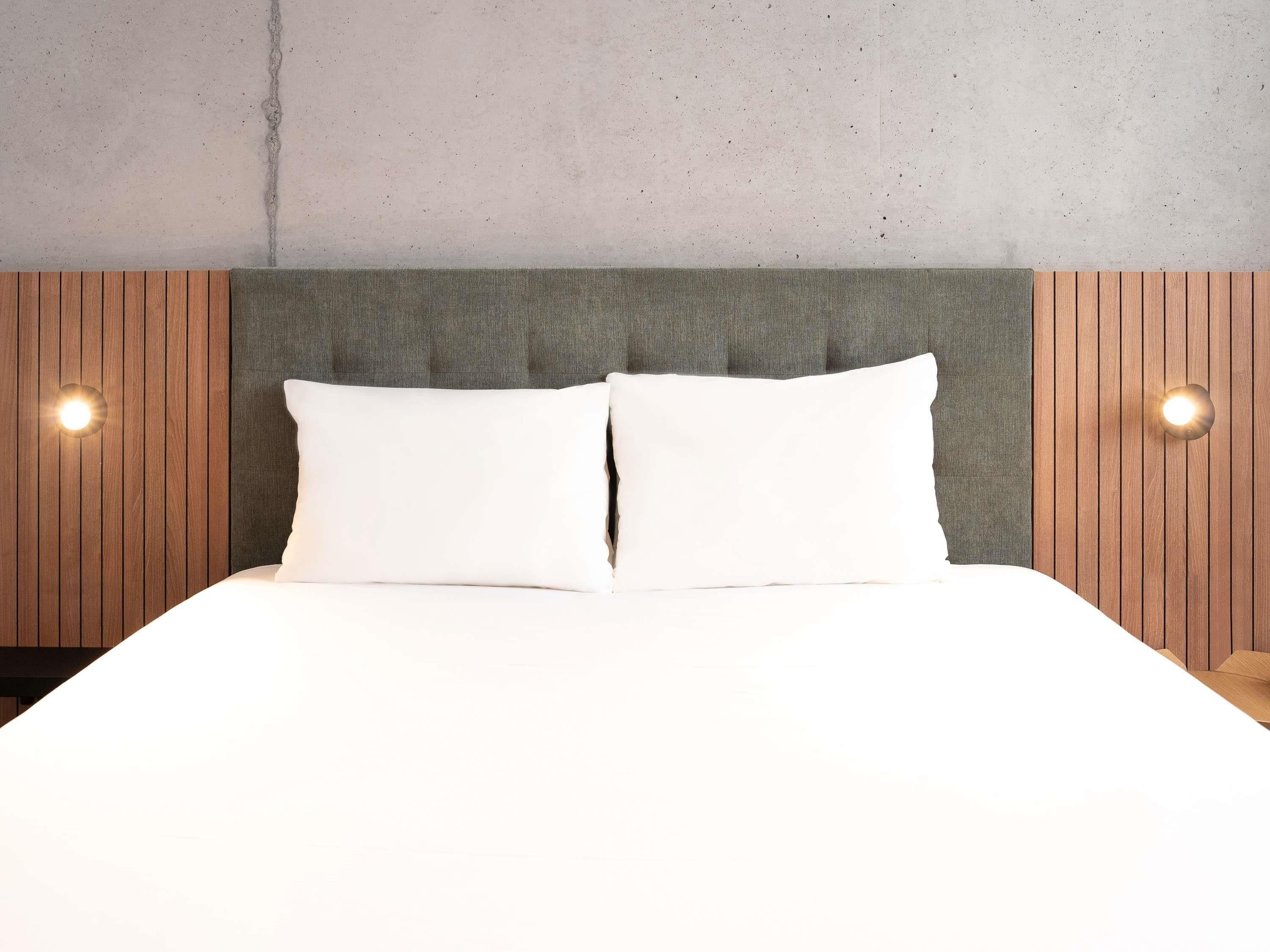A bed with two white pillows, a grey headboard, and wooden paneling on the sides.