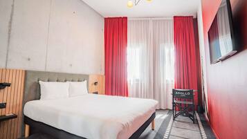 A hotel room with a bed, a TV, a chair, and a window with curtains.