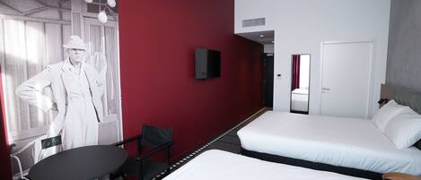 A hotel room with two beds, a TV, a chair, and a table.