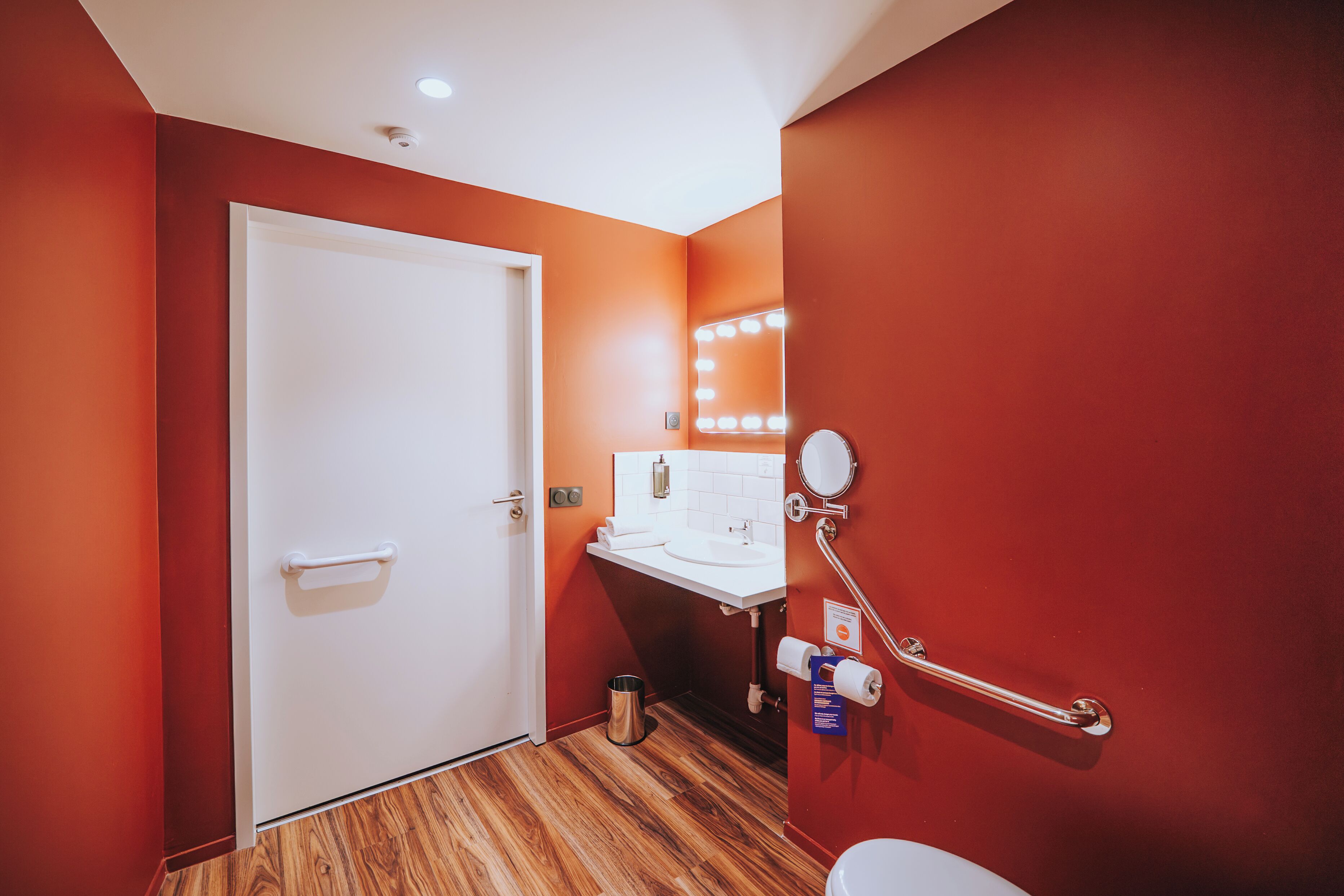 A bathroom with a white door, a sink with a mirror, and a handrail.