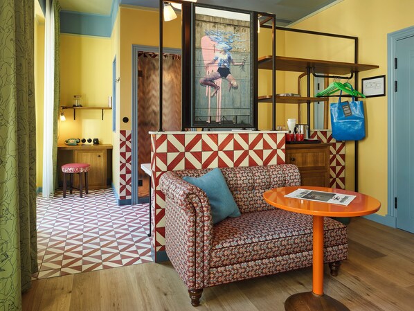 Una habitación con un sofá estampado, una mesita con una revista y una pared con un diseño geométrico.