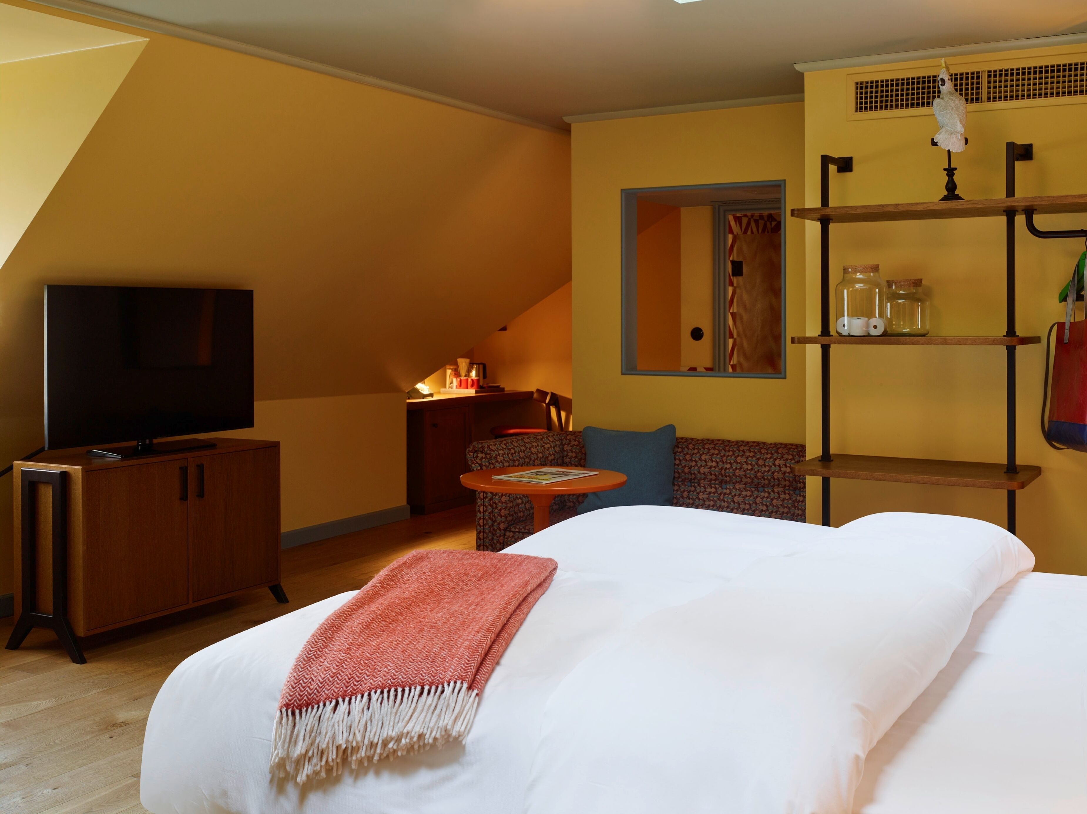 A bedroom with a bed, a TV, a small table, a sofa, and a shelf with jars.