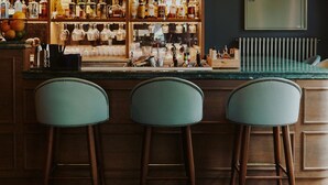A bar area with wooden stools, a countertop with bottles, and a hanging light fixture.