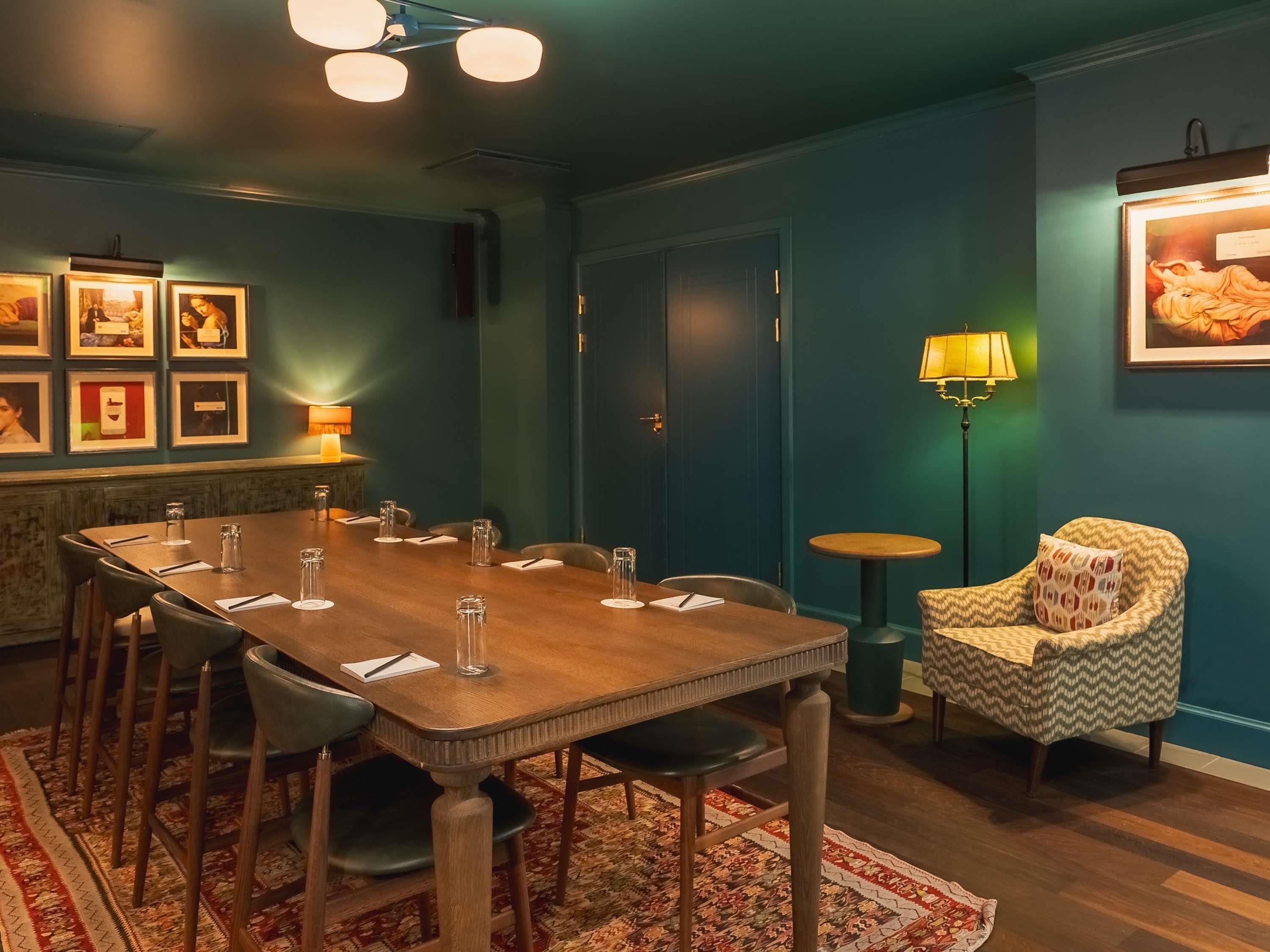 Ein Konferenzraum mit einem Holztisch, Stühlen, einem gemusterten Teppich, einem kleinen runden Tisch mit einer Lampe und einem gemusterten Sessel.