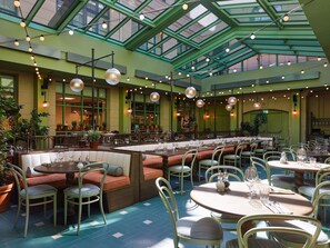 A spacious indoor dining area with high ceilings, green walls, and a glass roof. Tables are set with chairs, and there are potted plants around. - 25hours Hotel Indre By (Copenhagen)