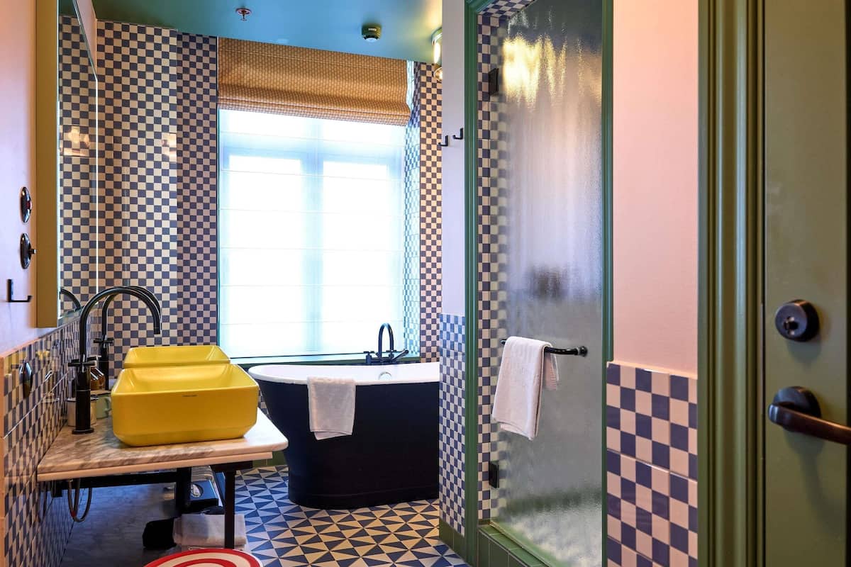 A bathroom with a checkered floor, a bathtub, a sink, and a window with curtains.