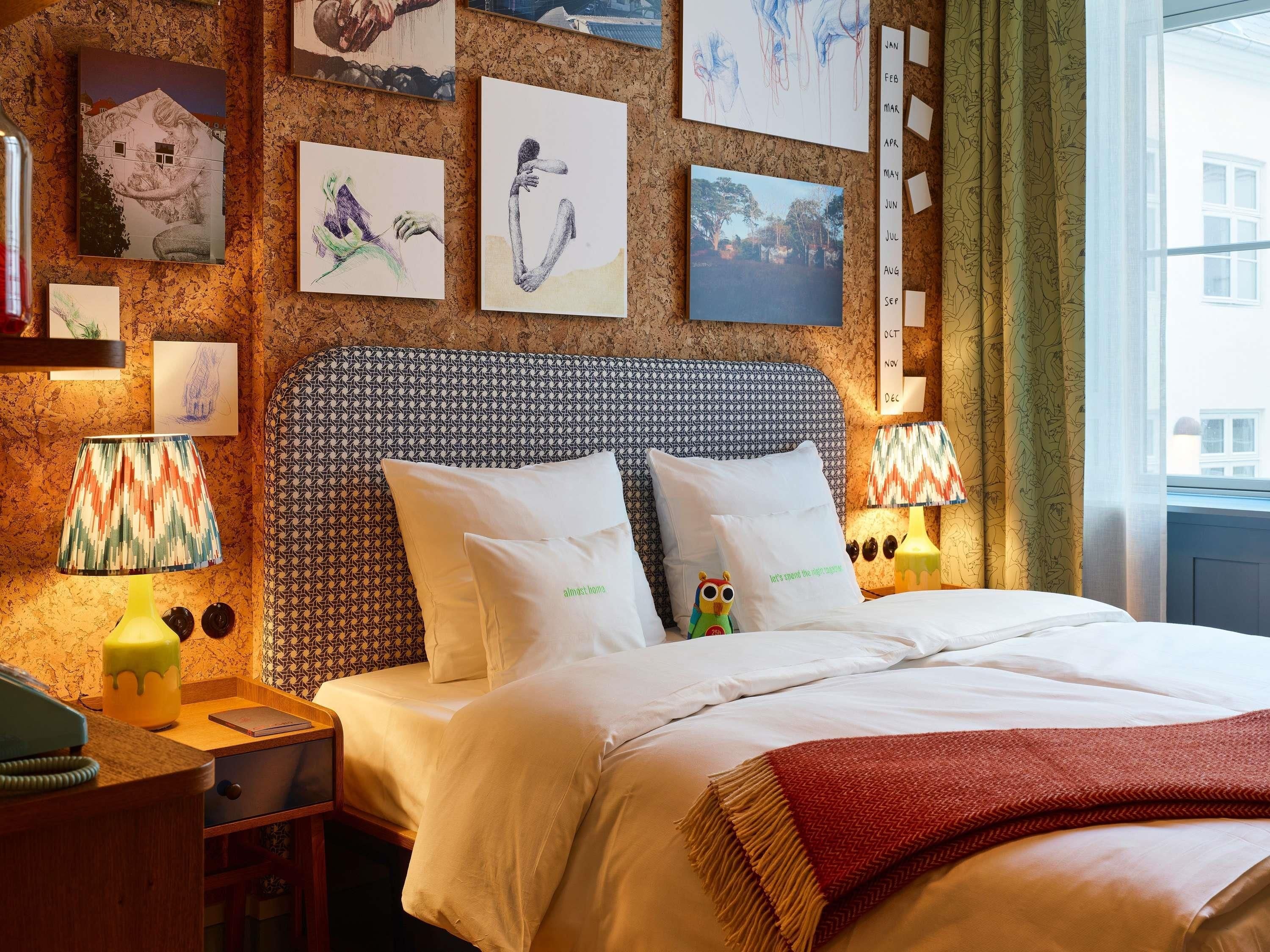 Una habitación de hotel con un cabecero estampado, una cama con ropa de cama blanca, una mesita de noche con lámpara y obras de arte en las paredes.