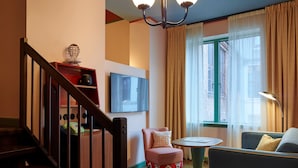 A living room with a staircase, a television, a window with curtains, and a sofa.