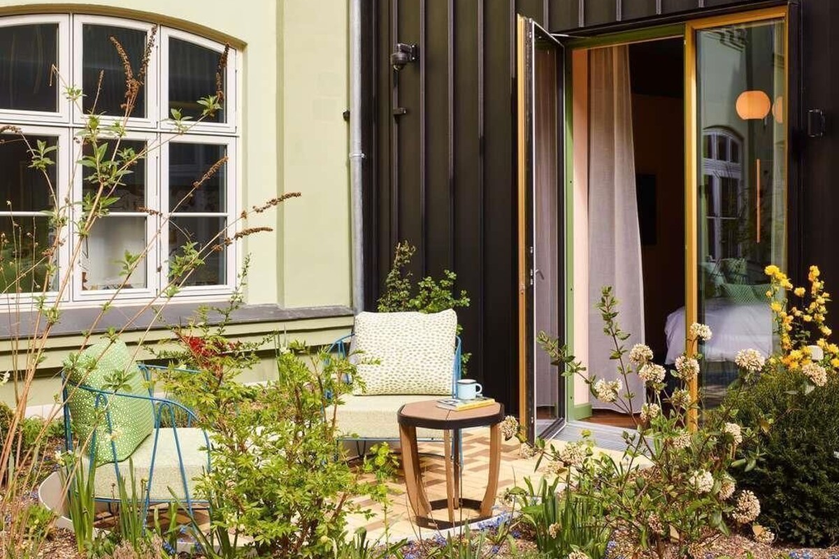 Cómodo espacio al aire libre con una mesa, sillas, una ventana con cortinas y una puerta de acceso al interior.