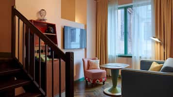 Un salon avec un escalier, un canapé, une petite table et un téléviseur fixé au mur.
