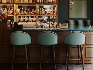 A bar area with wooden shelves stocked with bottles, a bar counter, and three bar stools. - 25hours Hotel Indre By (Copenhagen)