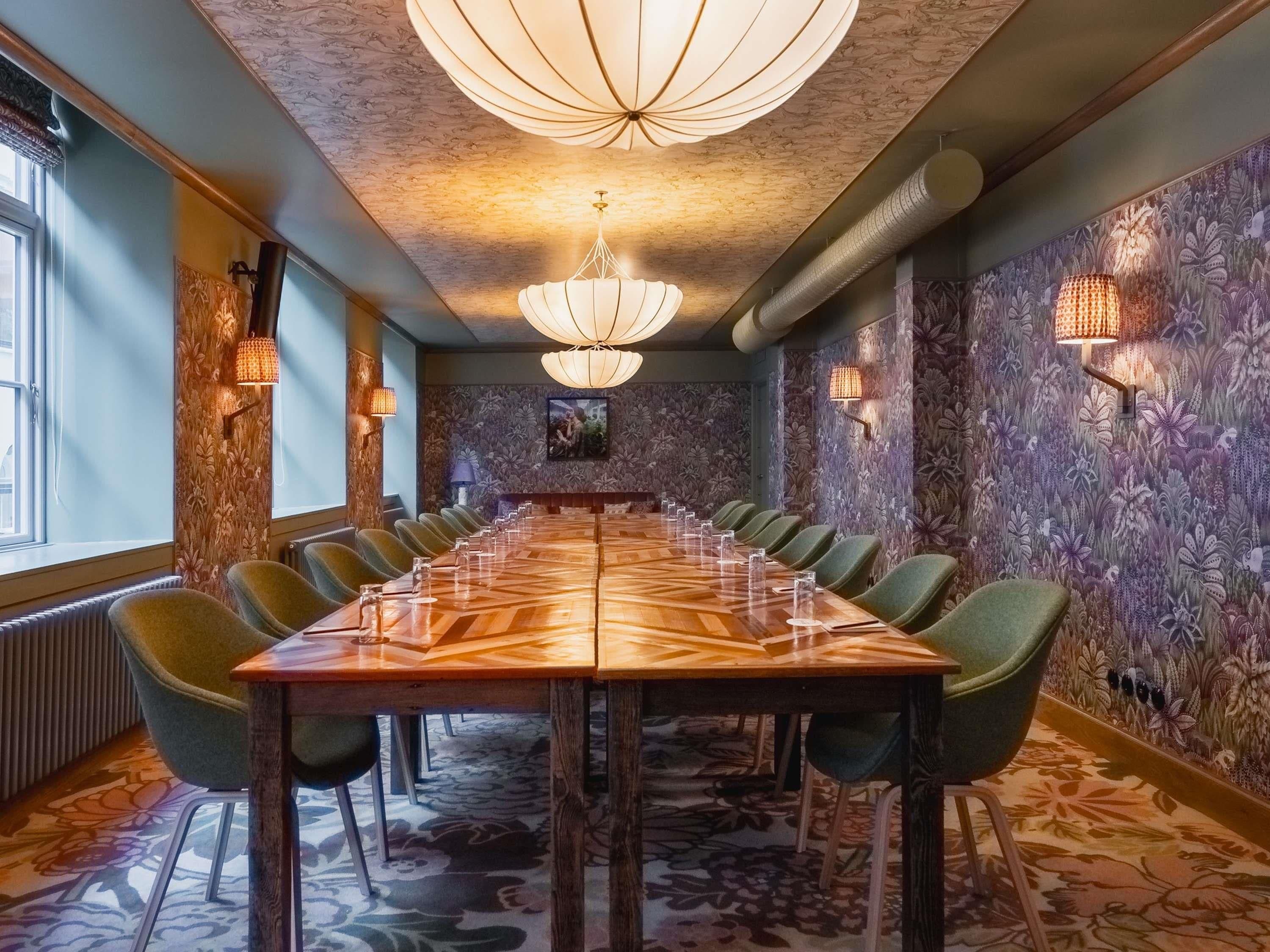 Un salón de conferencias con una larga mesa, sillas verdes y papel tapiz estampado.