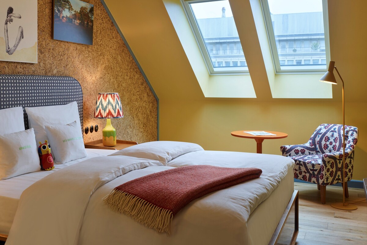 Un dormitorio con una cama, una silla, una lámpara y dos tragaluces.