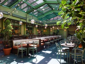 An indoor dining area with a high ceiling and green glass panels, featuring tables and chairs arranged for guests. - 25hours Hotel Indre By (Copenhagen)