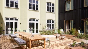 A courtyard with a wooden table and benches, surrounded by buildings with large windows and a garden area. - 25hours Hotel Indre By (Copenhagen)