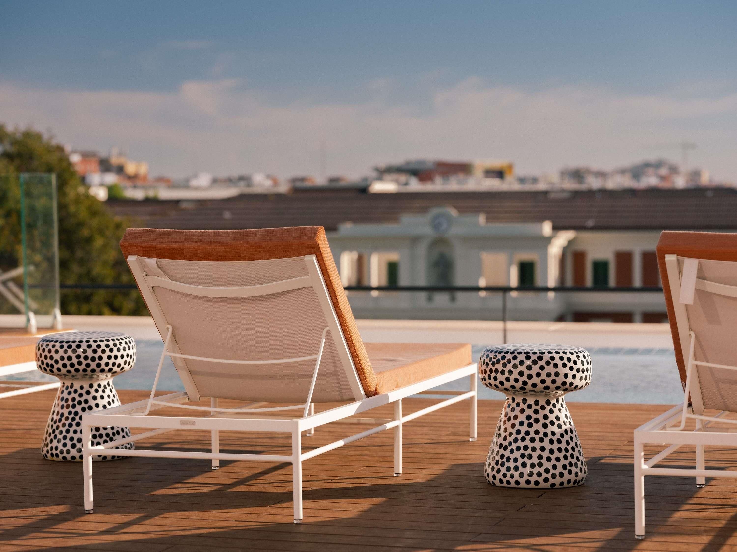 A poolside area with lounge chairs and stools, a clear view of the cityscape in the background.