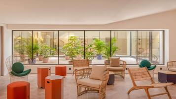 A spacious indoor area with wicker furniture, potted plants, and a large window providing a view of the outside.