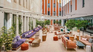 Een ruim buitengebied met banken, stoelen en tafels, omgeven door hoge gebouwen.