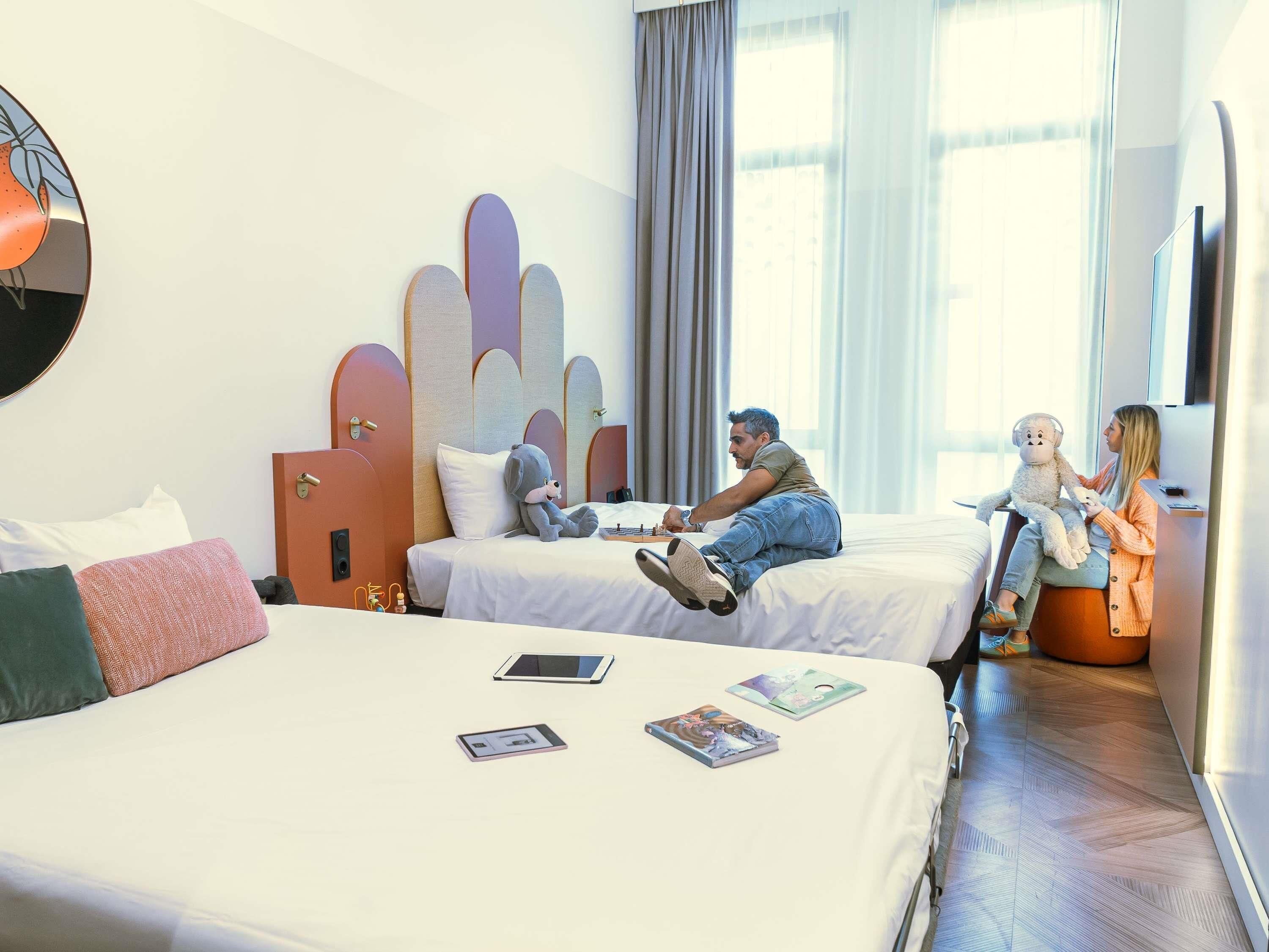 A hotel room with two beds, a large mirror, and a window with curtains.