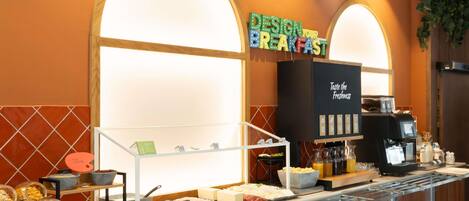 A breakfast buffet area with a coffee machine, various food items, and a sign that reads "DESIGN YOUR BREAKFAST".