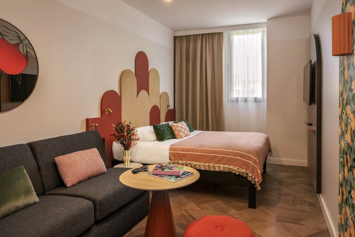 Un dormitorio moderno con cama, sofá, una mesita y un adorno en la pared.