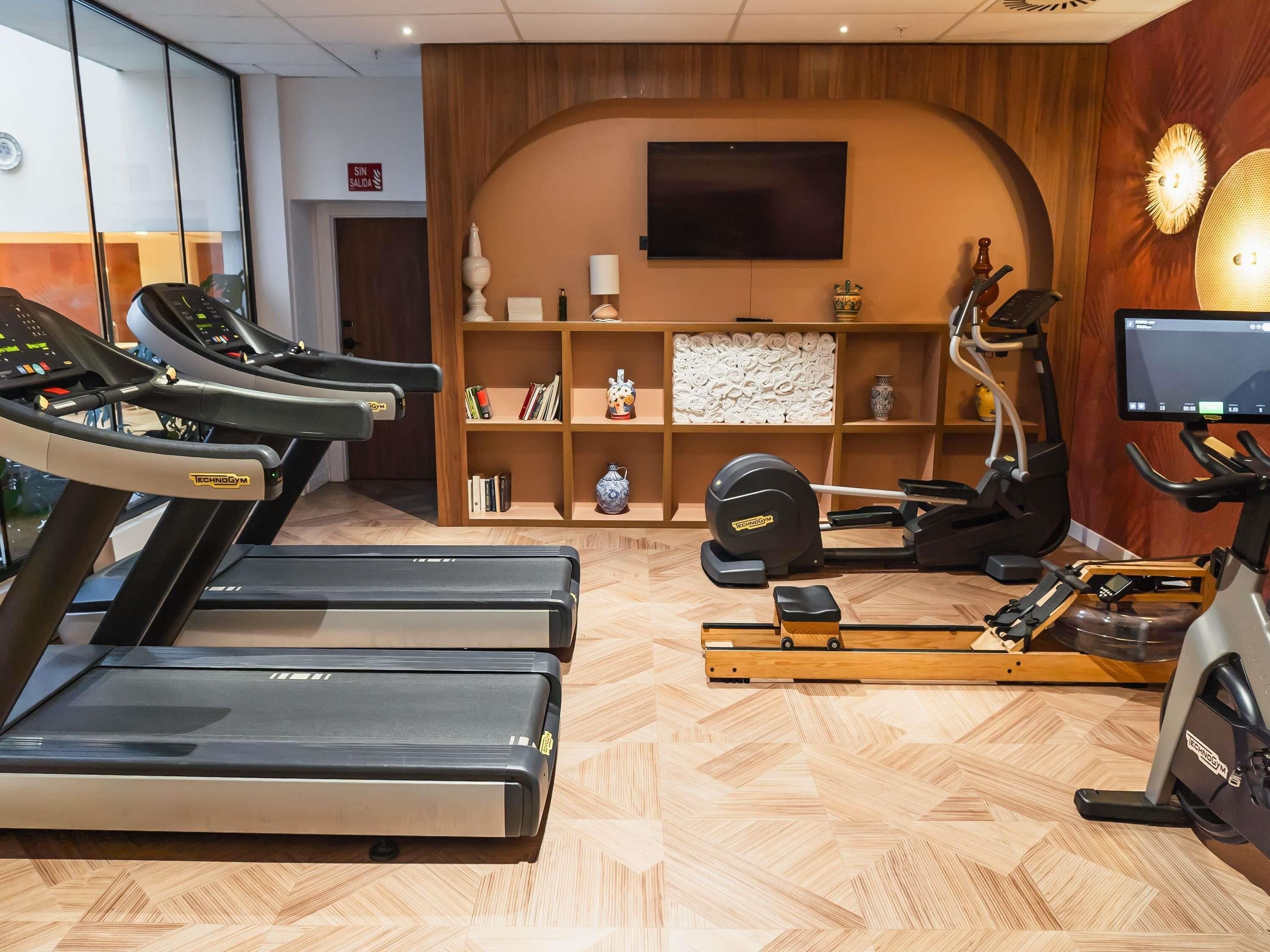 Un gimnasio con cintas de correr, una máquina de remo y una televisión instalada en la pared.
