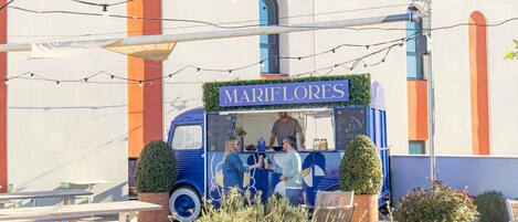 A food truck named 'MARIFLORES' with a blue and white color scheme, serving food, and located in an outdoor seating area with tables and chairs.