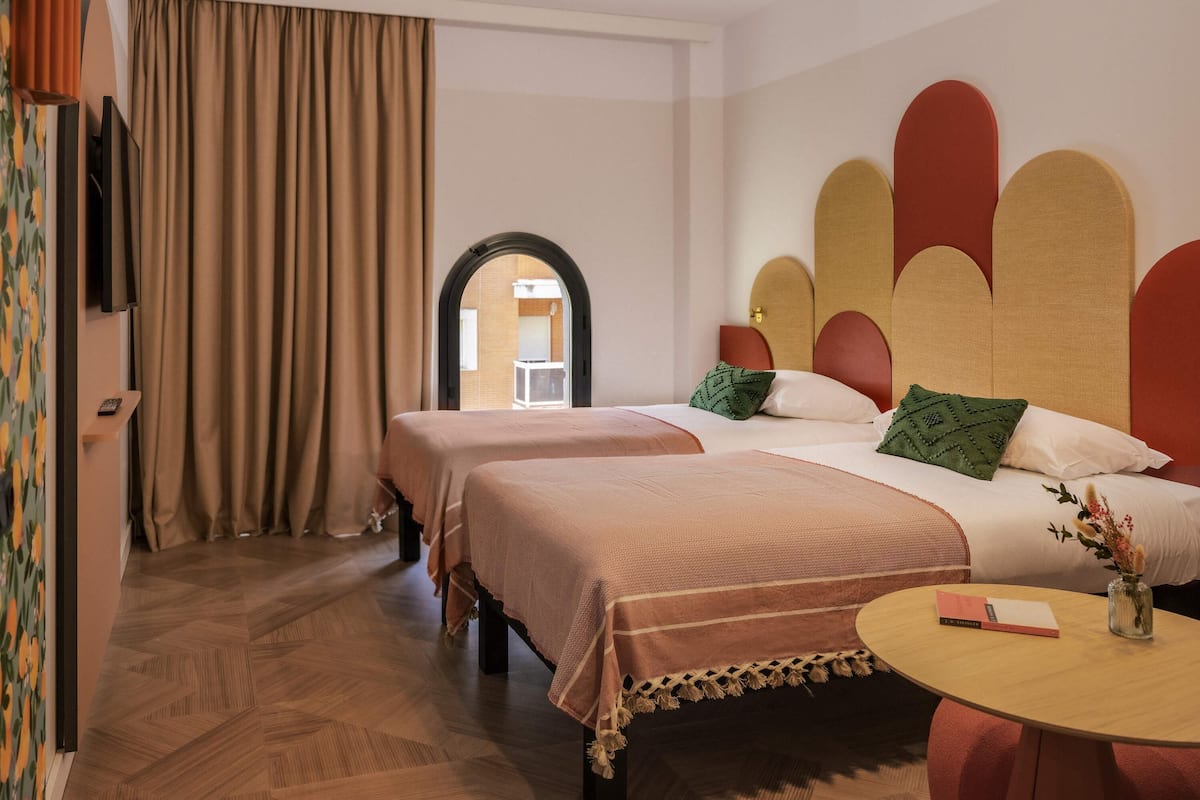 Habitación de hotel con dos camas, una mesa redonda y vistas a través de un arco.