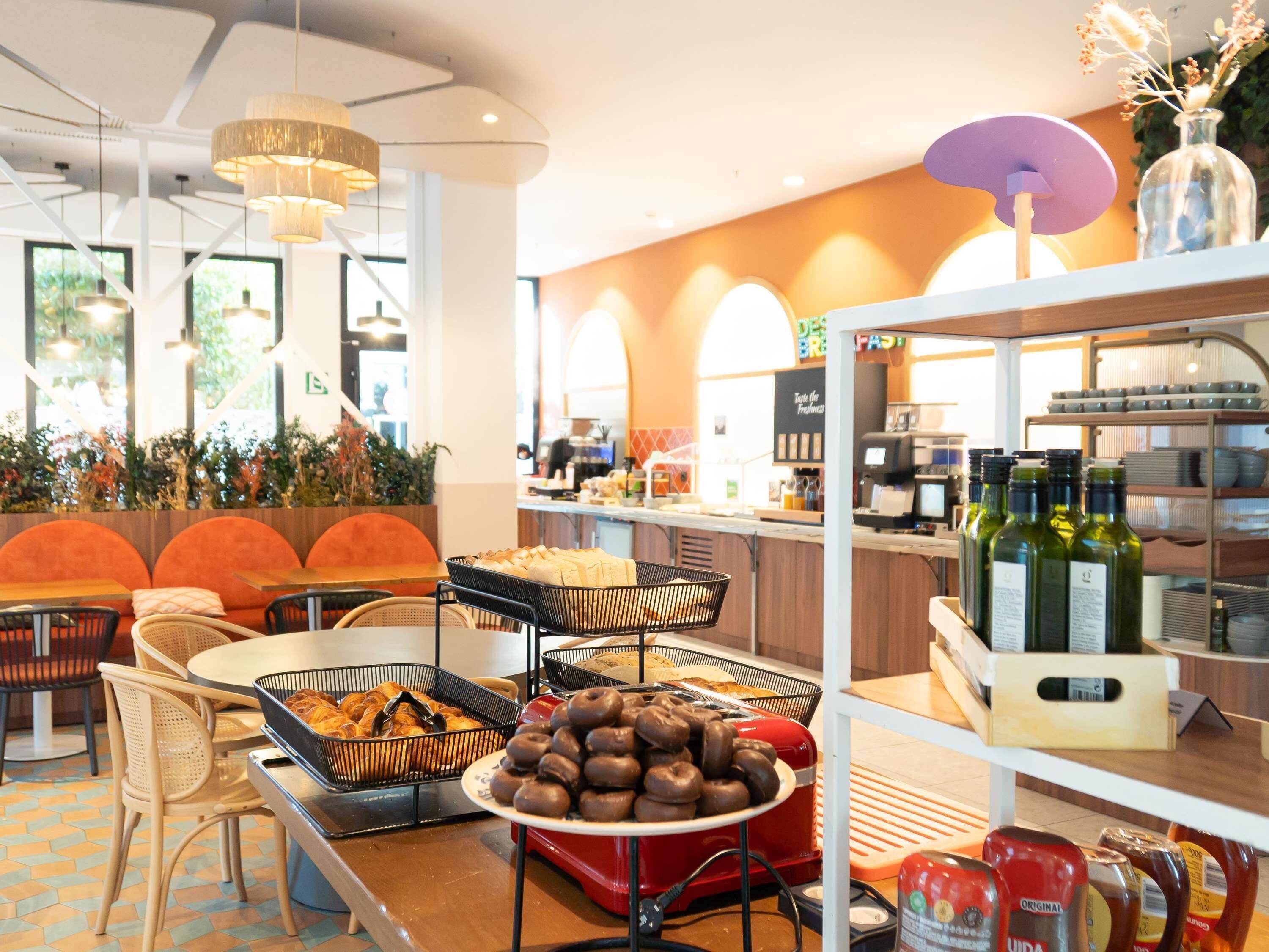 A cafe with seating, a buffet with pastries, and a bar area with bottles.