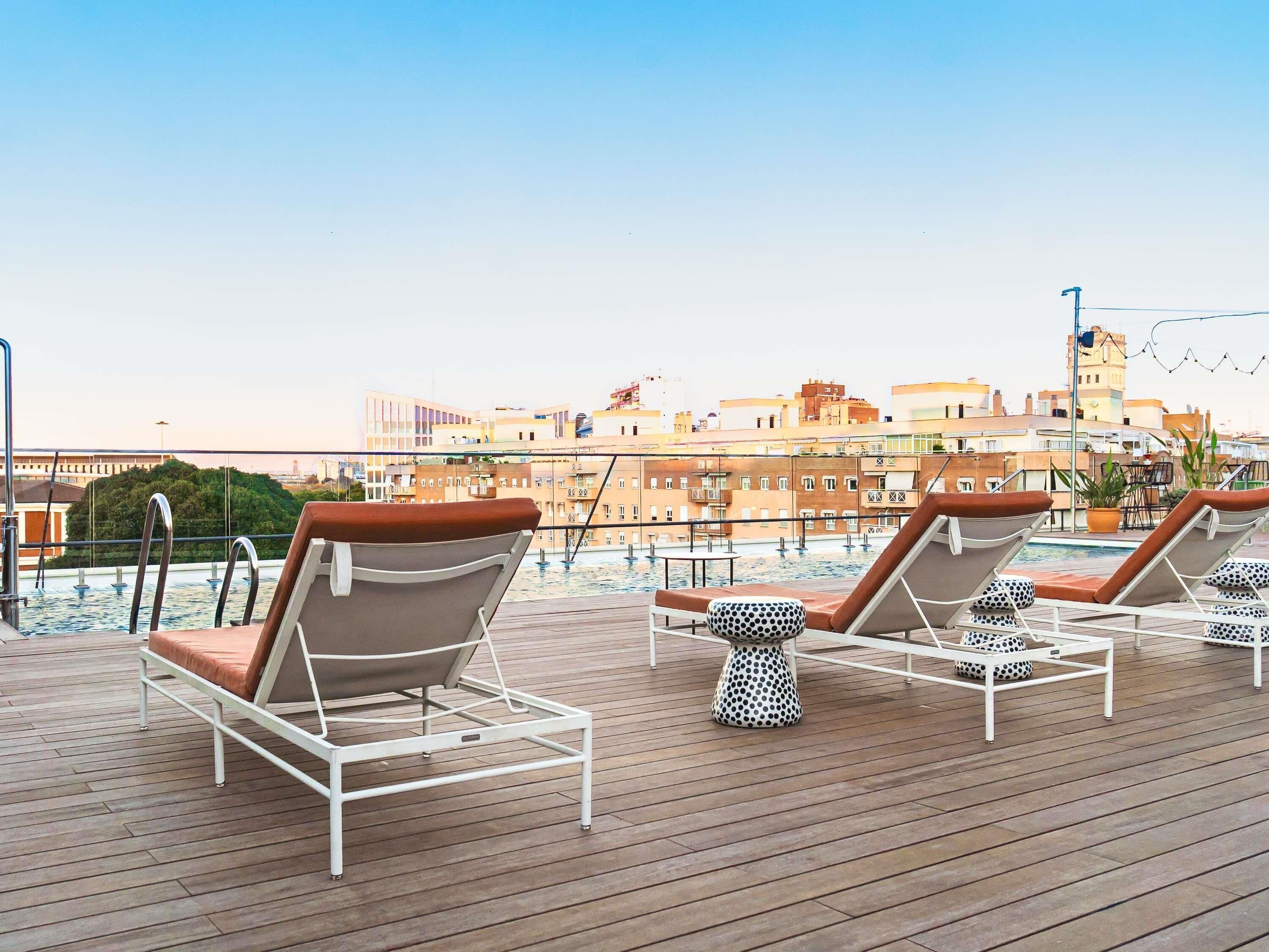 Un área de piscina en la azotea con sillones de descanso y vistas de la ciudad.