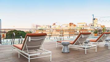 Un área de piscina en la azotea con sillones de descanso y vistas de la ciudad.