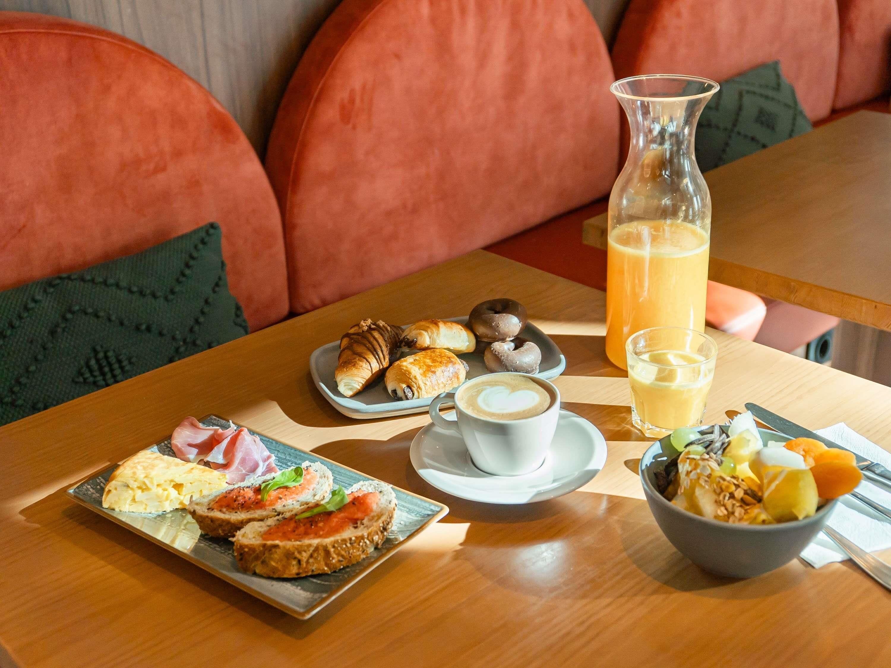 Ein Frühstückstisch mit Croissants, Gebäck, einer Kaffeetasse, einer Obstschale und einem Glas Orangensaft.