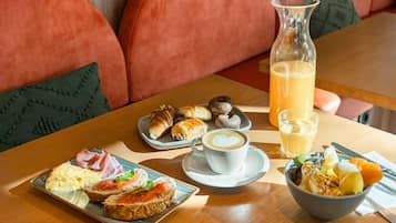 Ein Frühstückstisch mit Croissants, Gebäck, einer Kaffeetasse, einer Obstschale und einem Glas Orangensaft.