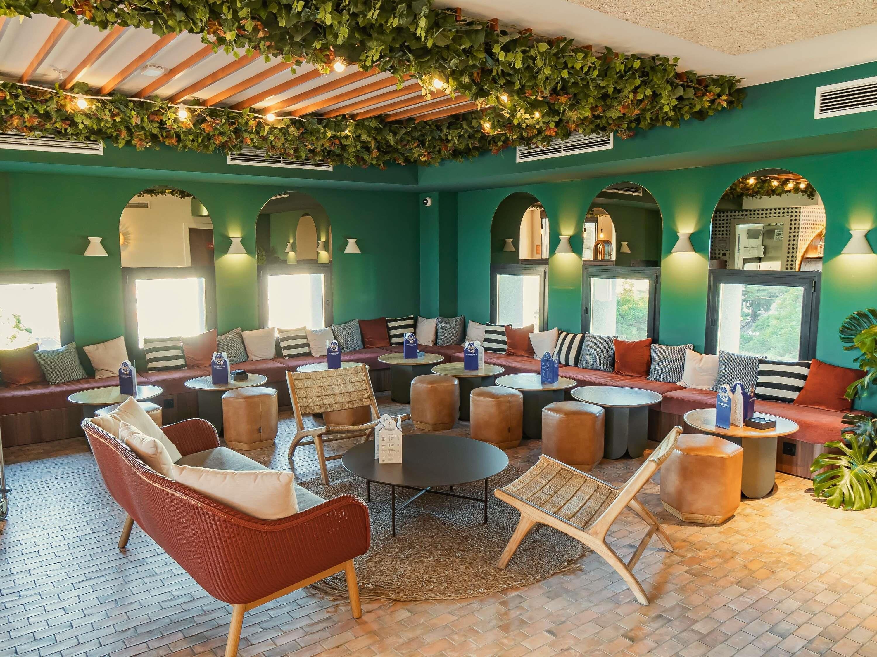 Cómoda zona de estar con asientos, mesas y un techo decorado con plantas e iluminación.
