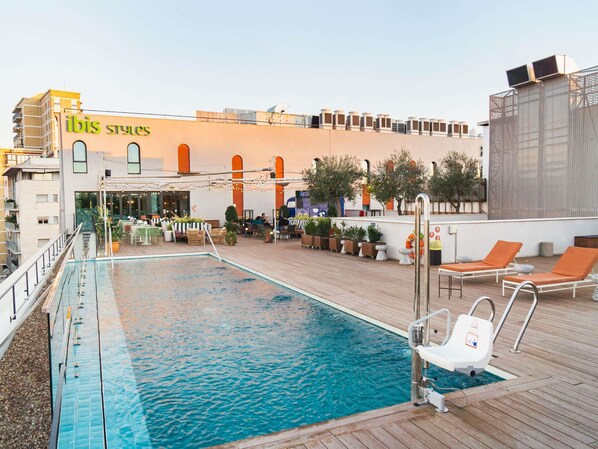 A rooftop pool area with lounge chairs, potted plants, and a building with 'ibis styles' signage. - Ibis Styles Sevilla Santa Justa (Seville)